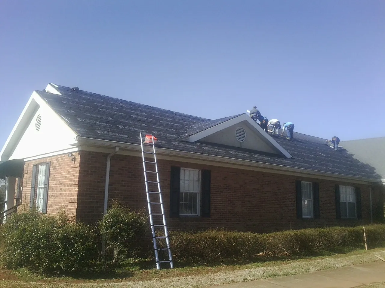 Crew tearing shingles off a brick ranch roof with a ladder set — Emergency Roof Repair work by our crew in Norcross