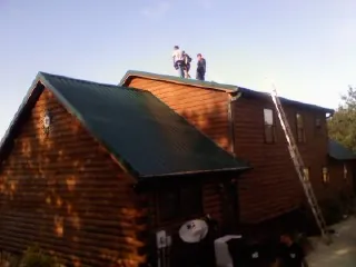 Crew on the ridge of a green metal roof on a two story log home in Norcross